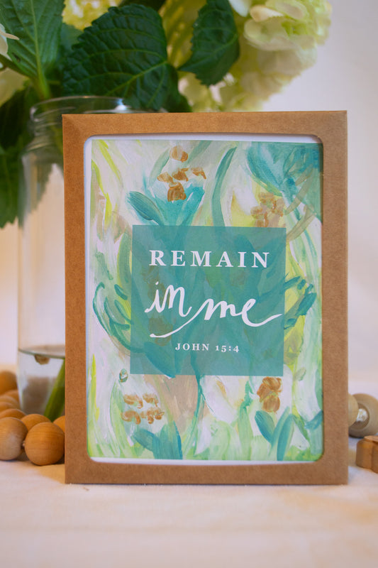 Framed print with floral design and 'Remain in me' text on a table with flowers in the background